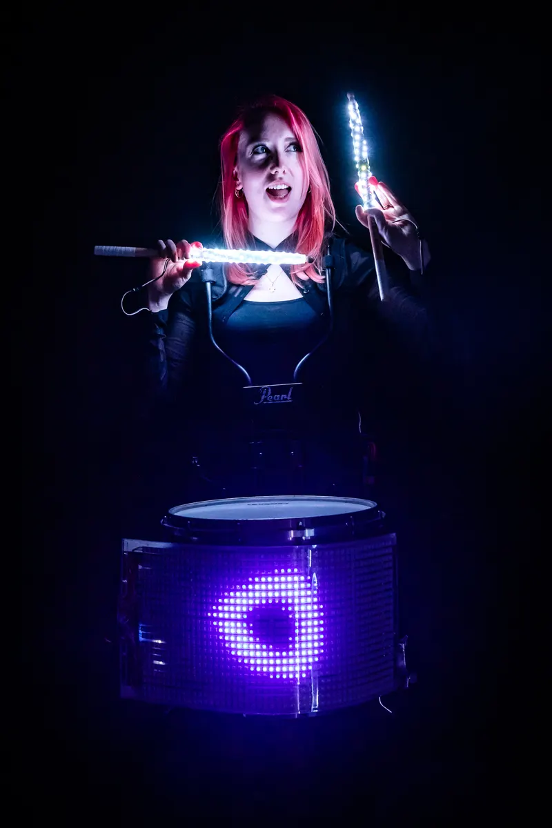 Drummer holds glowing sticks above an LED-lit drum.