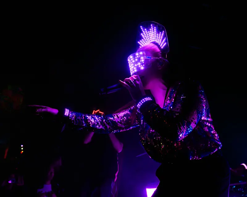 LED-masked vocalist sings into a microphone and reaches toward the crowd.