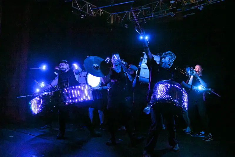 Flash Bang Brass drummers perform with LED drums under blue stage lights.