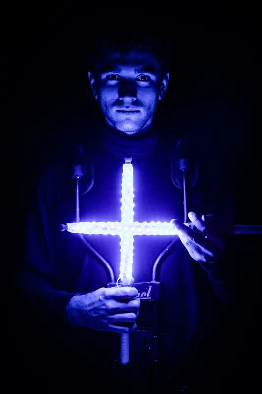 Drummer holds crossed glowing drumsticks in front of an illuminated drum.